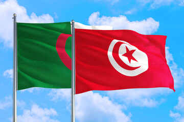 Fototapeta premium Tunisia and Algeria national flag waving in the windy deep blue sky. Diplomacy and international relations concept.