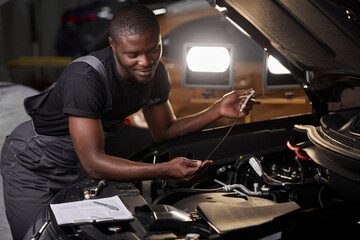 african professional auto service technician in uniform standing near car hood repairing and using...