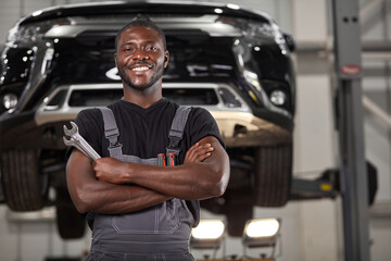 portrait of positive afro american auto mechanic in uniform posing after work, he is keen on...