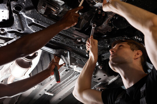 two friendly professional auto mechanic during work, they are successfully repairing car, solve problems together