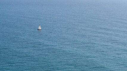 Sailboat sailing alone and in the distance in the middle of the sea on a sunny day