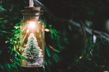 Christmas decoration. Hanging small Christmas tree in glass jar on pine branches christmas tree garland and ornaments over abstract bokeh