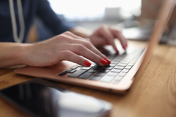 Business woman with red manicure is typing on laptop keyboard at table in office closeup. Remote homework concept.