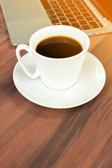 Coffee served in a cup, placed beside a portable computer. And have a pencil and notebook nearby