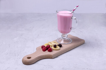 a glass of banana smoothie with raspberries and blackberries. next to the Board are pieces of...