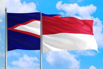 Monaco and American Samoa national flag waving in the windy deep blue sky. Diplomacy and...