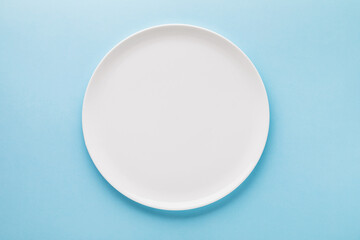 Empty white ceramic plate on a blue background, top view. Food background