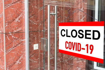 Close-up on a red closed sign in the window of a shop displaying the message "Closed due to Covid-19".