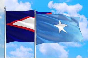 Somalia and American Samoa national flag waving in the windy deep blue sky. Diplomacy and...