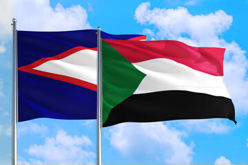 Fototapeta na wymiar Sudan and American Samoa national flag waving in the windy deep blue sky. Diplomacy and international relations concept.