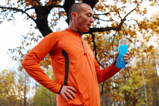 Male runner, athlete, drinks isotonic, energy drink after a hard workout in the open air. Sports nutrition