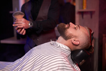 Fototapeta premium modern barber male begins to cut hair of client, making stylish beard, hair cut in salon, use brush