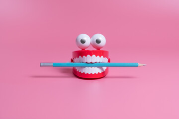 A plastic toy in the form of red jaws with white teeth and eyes holds a pencil between its teeth. Copywriting concept - obrazy, fototapety, plakaty