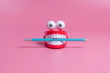 Fotobehang A plastic toy in the form of red jaws with white teeth and eyes holds a pencil between its teeth. Copywriting concept © the_mist