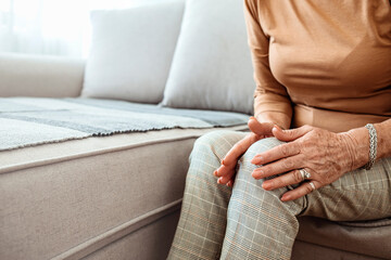 Elderly woman suffering from pain in knee at home, closeup. Health problems of old age. Senior woman suffering from pain in leg, massaging her knee at home, empty space
