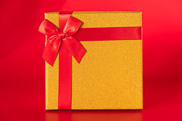 gold gift box with a red bow on a red background. Holiday gift for New Years, Christmas, Birthday or Valentine's Day