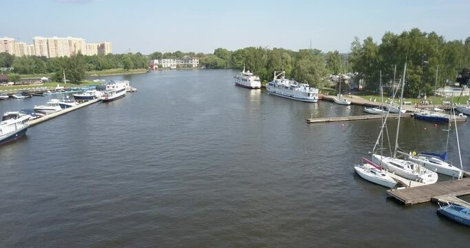 4K high quality calm windless bright summer morning aerial video of Moscow Channel yacht club embankment, green trees, wooden pier and shore with moored anchored boats and yachts near Moscow, Russia
