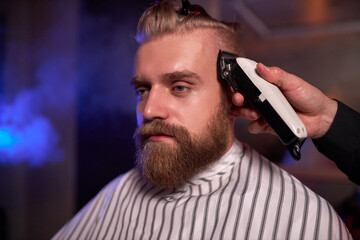 handsome caucasian man at the hairdresser in barber shop, barber male trimming hair to customer with electric razor at barbershop