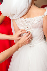 Obraz na płótnie Canvas bridesmaid buttoning the dress on bride, details of beautiful lace wedding dress
