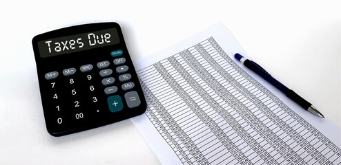 The word taxes due on the calculator.A sheet of paper with a table and numbers, a pen on a white background.