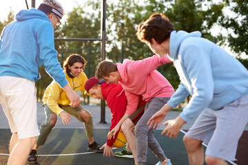 Obraz premium group of young male teenagers in colourful hoodies playing basketball outdoors in the street