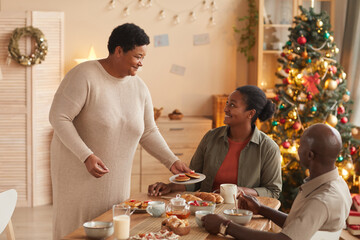 Portrait of senior African-American woman serving homemade food for family at breakfast and smiling happily