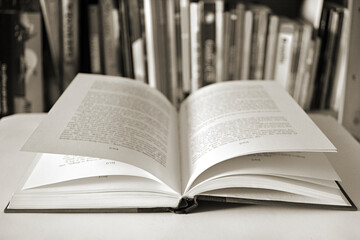 Black and white close up of an open book with bookshelf on background.