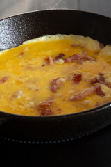 Omelette, with bacon, cooking on an electric hob or stove in a cast iron frying pan