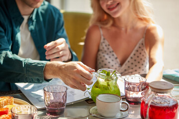 male is going to pour sweet beverage into glasses for woman in light cafe, drink.