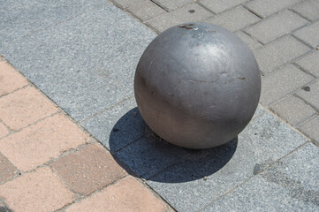 Fototapeta na wymiar sphere-shaped metal black bollard isolated, casting its shadow on concrete floor in the street