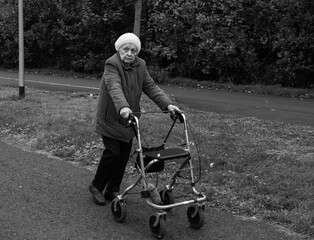 Obraz premium Elderly woman taking a walk in winter with the help of a walker aid in black and white