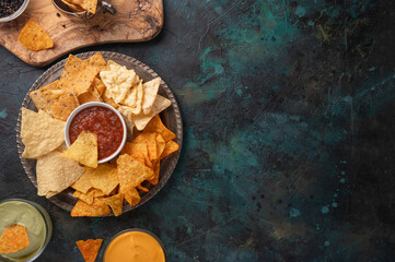 Appetizing corn tortilla chips on dark blue marble background. Salsa, cheese dip and avocado souse for taste. Unhealthy food. Traditional mexican dish. View from above. Flat lay.
