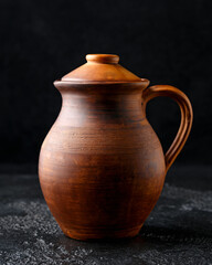 rustic handmade brown clay jug with lid on black background