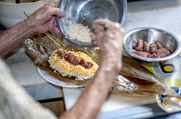 Elderly member making Glutinous Sticky Rice Dumplings ( Zong in Chinese ) at home for family during festival, glutinous rice stuffed with different fillings and wrapped in bamboo leaves. 