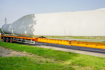 A view of a truck, a low-loader semi-trailer with oversized wind generator parts in the parking lot