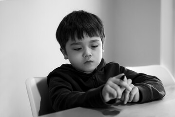 Black and white portrait Bored child siting alone table with unhappy face, Tired kid lookig down deep in throught, Lonely Young boy with sad face looking at his hands, Health metal concept