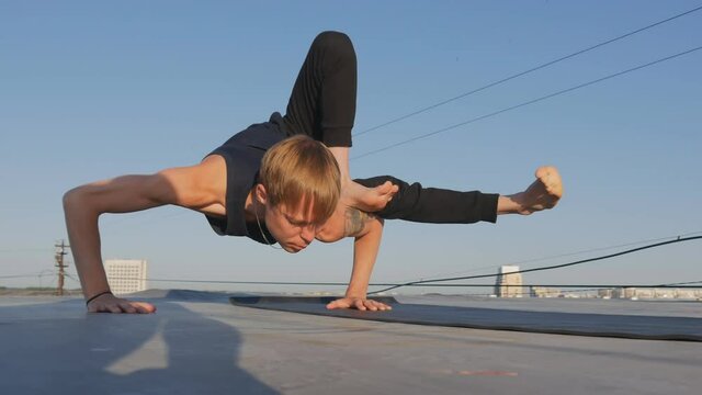 a strong and handsome Caucasian guy performs a difficult yoga assan. Stands on hands and the body is horizontal parallel to the floor, bent to the side. Health