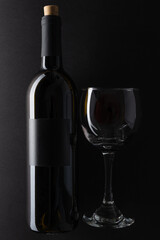 Elegant bottle and wineglass of red wine on black background. Top view. Concept of advertising and promotion of alcoholic drinks. Space for text.