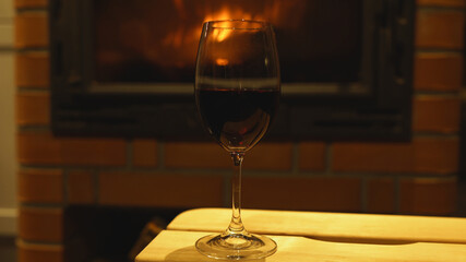 Glass of red wine standing by the fireplace.
