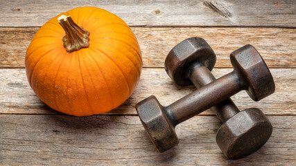 a pair of vintage iron rusty dumbbells on a rustic barn wood background with a pumpkin, fitness during fall holidays concept