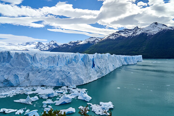 Fototapeta na wymiar Blue ice of Perito Moreno Glacier in Glaciers national park in Patagonia, Argentina with turquoise water of Lago Argentino in the foreground, dark green forests and sow covered mountains of the Andes