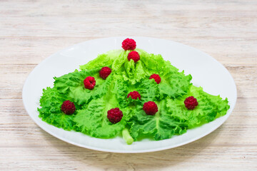 The Christmas tree is lined with green lettuce leaves, decorated with red raspberries on a white plate. Food for the New Year. Table decoration.
