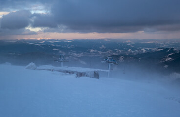 Alpine resortr ski lift with seats going over the sunset mountain skiing  slopes in extremally windy weather
