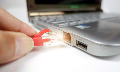 Man's hand connects the cable to the laptop. - obrazy, fototapety, plakaty