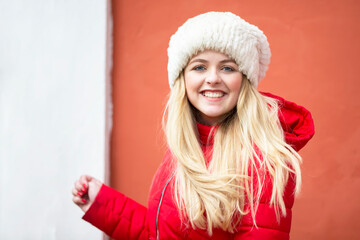 Portrait of a beautiful blonde girl in a warm hat and red jacket.