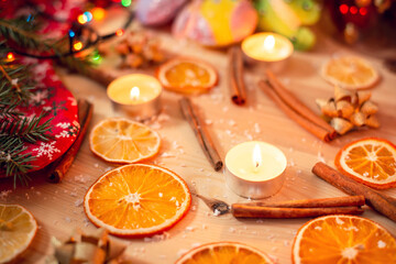 Dried orange slices, cinnamon sticks and small aromatic candles on the table close-up. Christmas time, warm festive atmosphere.