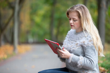 Obraz premium Young beautiful woman in the park with a tablet or e-book.