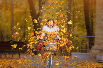 Young beautiful woman rides a bicycle in an autumn park under falling leaves.