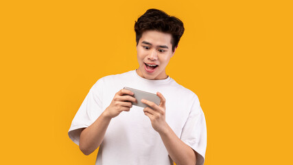 Excited asian man playing mobile games on orange background