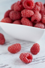Raspberries in a white bowl on a white wooden table.